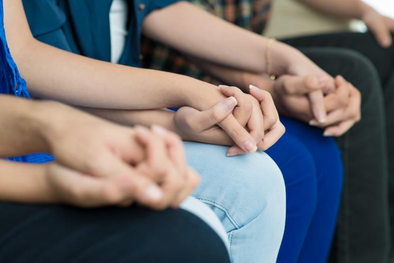 A close-up of four causcasian people sitting in a row, holding hands