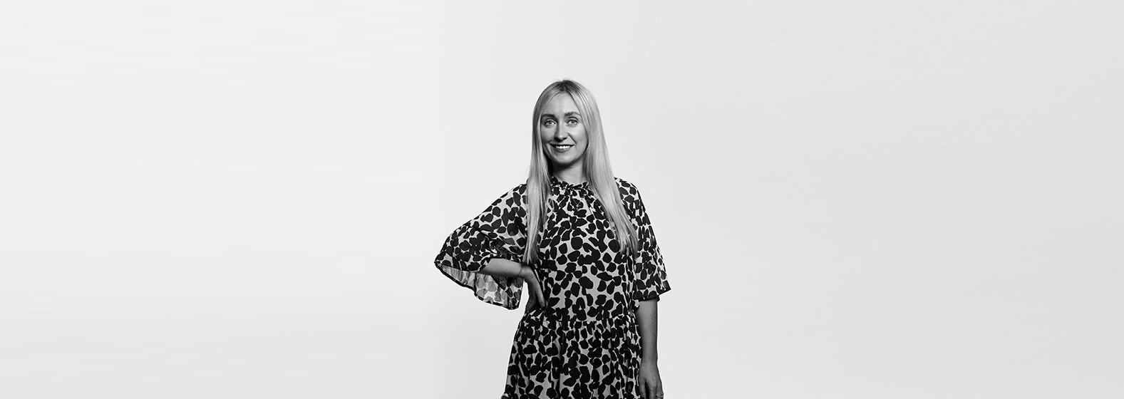 A greyscale photo of Grace McNamara. She has long blonde hair, is wearing a black blazer and a white blouse. She is smiling