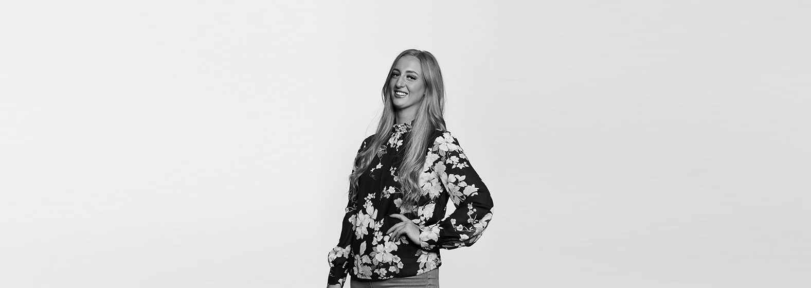 A greyscale photo of Yvette Beddows, Team Administrator in our Court of Protection department. She is wearing a floral blouse, has one hand on her hip and is smiling.