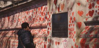 A Black woman draws a memorial heart on the Covid-19 Memorial Wall. The wall is covered in red hearts, dedicated to people lost as result of Covid.