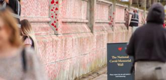 The Covid Memorial Wall covered in red heart drawings. People are walking past.