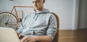 A Caucasian man sits at a laptop and looks at the screen.