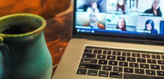 A laptop with a Zoom meeting on the screen is on a desk with a blue antique looking mug to the left of it