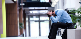 A man sits on a bench with his head in his hands.