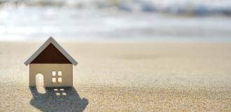 A cutout of a house on some sand in front of some waves