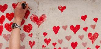 Person putting a red heart on a concrete wall