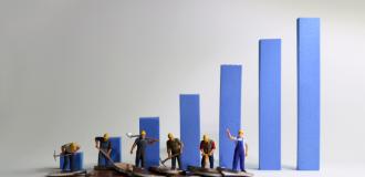 Small models of workers shovelling coins in front of blue bar charts. 