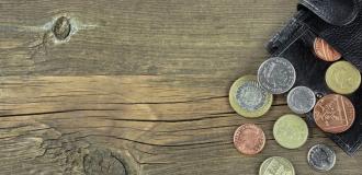 Pound and penny coins spill out of a dark leather wallet onto a wooden floor.