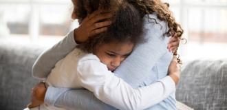 A photo of a young girl looking sad and hugging her mum.