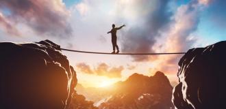 A person balancing on a tight rope between two boulders