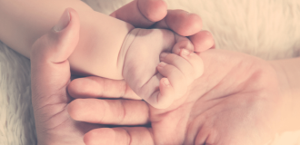 A pair of new parents gently hold their newborn baby's hand