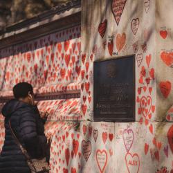 A Black woman draws a memorial heart on the Covid-19 Memorial Wall. The wall is covered in red hearts, dedicated to people lost as result of Covid.