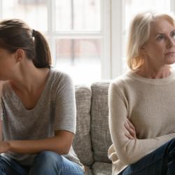 Two white women, one older and one younger, sit facing away from each other on a sofa.