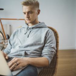 A Caucasian man sits at a laptop and looks at the screen.