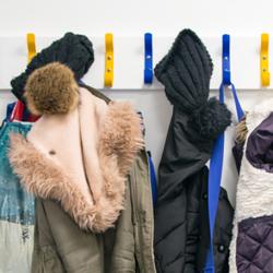 A row of school children's coats and bags hang on coat hooks.