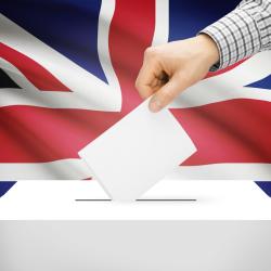 A hand places a paper in a ballot box in front of the Union Jack.