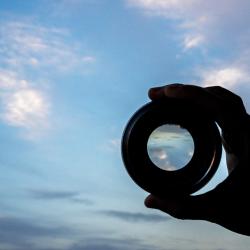 hand holding a camera lens to the sky, symbolising the need for transparency 