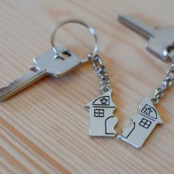 2 sets of keys lay on a wooden table. Each key has 1 half of a 'broken house' keyring that, when put together, make a complete house.