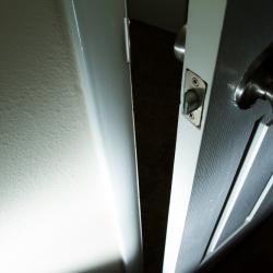 A down-angled close up of a door that is slightly ajar. The hallway beyond the door cannot be looked into, the photo is very shadowy and looks menacing.