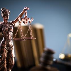 A small bronze statue of Justice holding the scales and the sword is in the foreground. There are books and a set of scales in the blurry background.