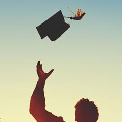 Silhouette of graduates throwing their mortar boards into the air against a blue sky.