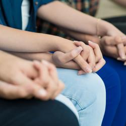 Three people holding hands while sitting down.