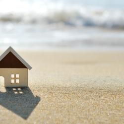 A cutout of a house on some sand in front of some waves