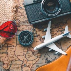 hat, model aeroplane, passports and other holiday themed items lying on a world map