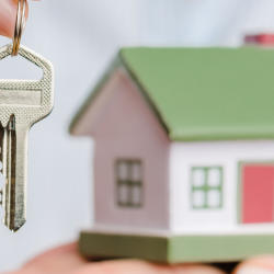 small toy house with a house key being held in front of it