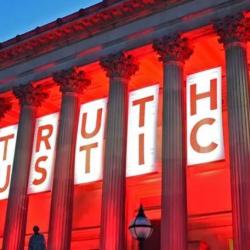 St George's Hall Liverpool, lit up red with "Truth" and "Justice" banner behind the buildings columns. 