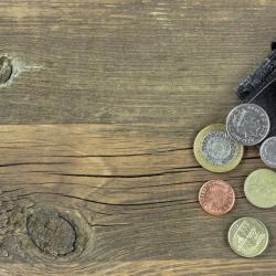 Pound and penny coins spill out of a dark leather wallet onto a wooden floor.