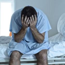 A man sits on a hospital bed with his head in his hands. 