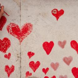 A white hand colours in a red heart on the National Covid Memorial Wall