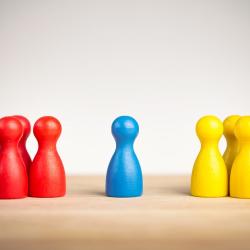 A group of red game pieces are standing opposite a group of yellow game pieces. A single blue game piece stands between the two groups.