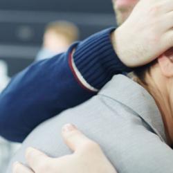 A man comforting a woman as she cries into a tissue.