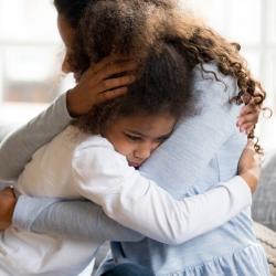 A photo of a young girl looking sad and hugging her mum.