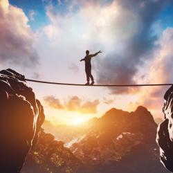 A person balancing on a tight rope between two boulders