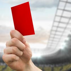 A red card is held up to a cloudy sky on the grounds of a football stadium.